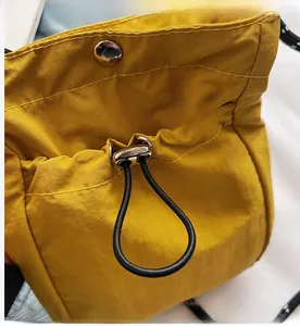Detail of yellow nylon crossbody bag featuring secure drawstring and metal snap closure