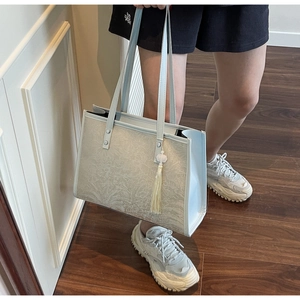 Detail of light blue tote bag with floral texture and tassel, showing capacity on arm