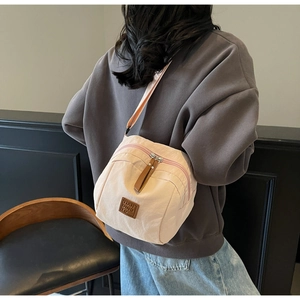 Détail du sac bandoulière en nylon pêche montrant l'écusson en cuir et la fermeture éclair