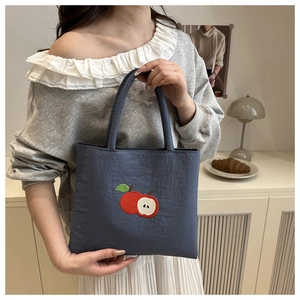 Detail of navy nylon tote bag featuring red apple embroidery and textured fabric
