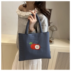 Detail of navy blue tote bag featuring red apple embroidery on textured pleated fabric