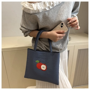 Detail of navy blue nylon tote bag with red apple embroidery and textured fabric