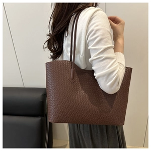 Detail of a large brown woven tote bag showing leather texture and shoulder strap design
