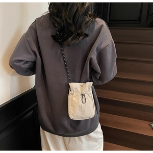 Detail of beige nylon crossbody bag with woven drawstring and adjustable strap on a model