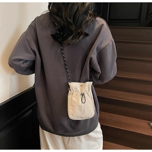 Detail of a beige drawstring crossbody bag with adjustable black strap on a model