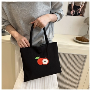 Close-up of black canvas tote bag featuring delicate red apple embroidery design
