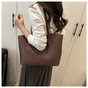 Detail of woven texture on dark brown leather tote bag worn by a model in soft light