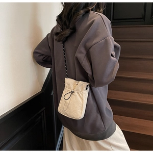 Detail of beige nylon drawstring crossbody phone bag with black cord shoulder strap
