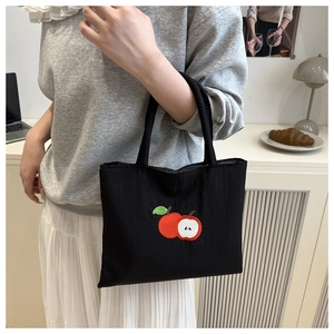 Close-up of black canvas tote bag featuring vibrant red apple embroidery details