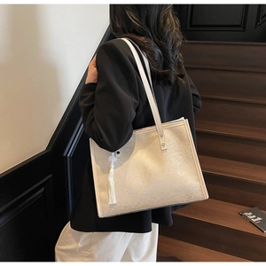 Detail of off-white tote bag featuring delicate floral texture and white tassel pendant