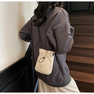 Close-up of beige drawstring crossbody phone bag with black cord strap and spring buckle