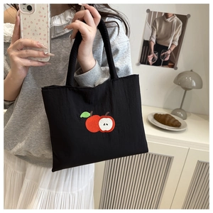 Close-up of a compact black nylon tote with apple embroidery shown in a lifestyle setting