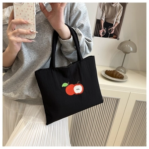 Detail of a black canvas tote bag featuring a minimalist red and green apple embroidery