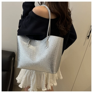 Close-up of a large silver metallic woven tote bag with glossy embossed texture worn by a model