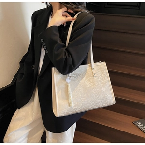 Detail of cream tote bag with embossed floral texture and a decorative tassel pendant