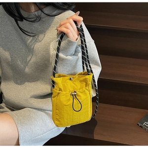 Detail of yellow nylon crossbody phone bag with black drawstring and woven rope strap