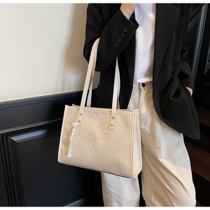 Detail of off-white tote bag featuring embossed floral patterns and a tassel charm