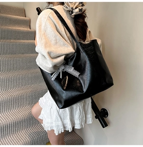 Detail of black faux leather tote bag featuring a white lace bow and pearl pendant