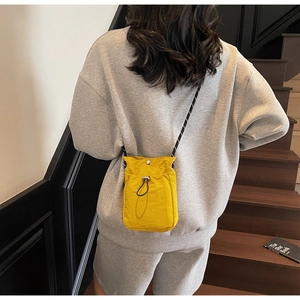 Detail of yellow nylon crossbody phone bag with black cord strap and drawstring pocket