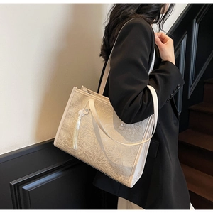 Detail of cream tote bag featuring floral jacquard patterns and a soft tassel charm