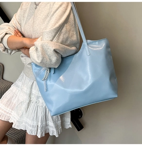 Detail of light blue tote bag with shiny synthetic leather and pearl lace charm accessory