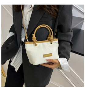 Detail of cream woven bucket bag with brown leather handles worn by a model in a suit