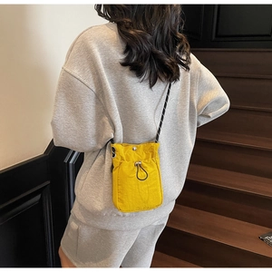 Detail of a bright yellow nylon crossbody phone bag with black drawstring pocket and strap