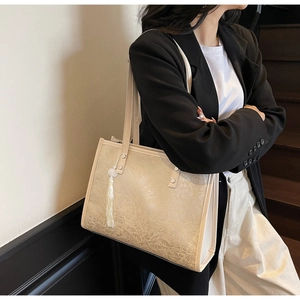 Detail of beige jacquard tote bag featuring floral texture and a white silky tassel charm