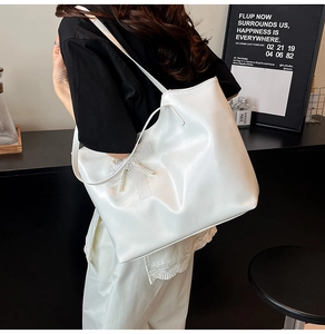 Detail of white leather tote bag featuring lace bow and pearl decoration on shoulder
