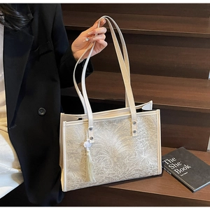 Detail of off-white tote bag featuring palm leaf embossing and tassel charm on double straps