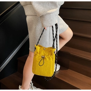 Detail of yellow nylon crossbody bag with woven rope strap on wooden steps