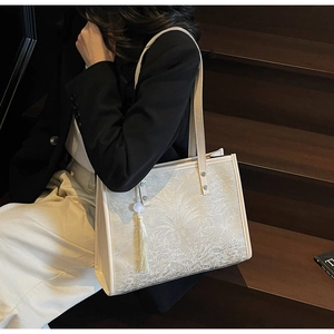 Detail of cream tote bag featuring embossed leaf textures and elegant fringe tassel detail