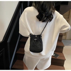 Detail of minimalist black nylon drawstring crossbody bag with textured shoulder strap