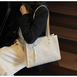 Detail of cream jacquard tote bag with tropical leaf pattern and tassel accessory