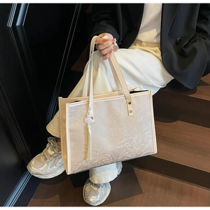 Close-up of beige jacquard tote bag with botanical texture and tassel charm