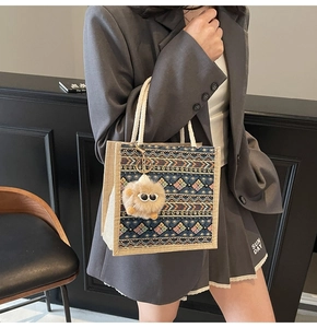 Close-up of ethnic style tote bag with woven straps and plush eye charm on grey suit