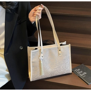 Detail of beige tote bag with embossed floral texture and decorative yellow tassel