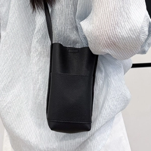 Minimalistische schwarze Mini-Umhängetasche aus Kieselleder an der Schulter eines Models