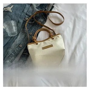 Detail of woven straw bucket bag with brown leather handles and adjustable shoulder strap