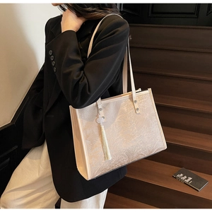 Detail showing high-quality floral jacquard texture and tassel on cream tote bag
