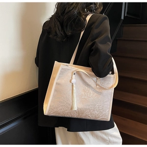 Detail of beige tote bag featuring floral jacquard texture and white tassel pendant