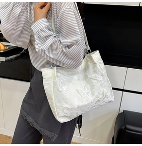Detail view of a white satin shoulder bag with 3D lace butterfly appliques and slim strap