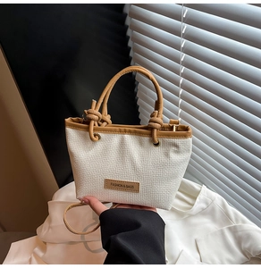 Detail of woven straw handbag with brown leather trim and knotted dual handles