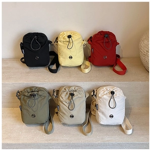 Mini nylon drawstring crossbody bags in six vibrant colors displayed on stone steps