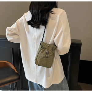 Detail of olive green nylon drawstring crossbody bag with textured fabric and thin cord strap