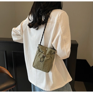 Close-up of olive green nylon crossbody bag with drawstring and woven shoulder strap