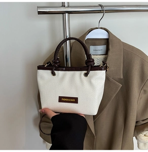 Detail of hand-woven bucket bag with retro knotted handle and metal fashion logo
