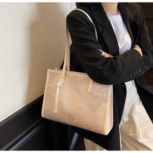 Detail of beige tote bag featuring floral jacquard texture and white tassel charm