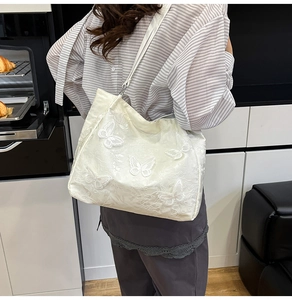 Detail of white underarm bag featuring 3D butterfly embroidery and floral lace texture