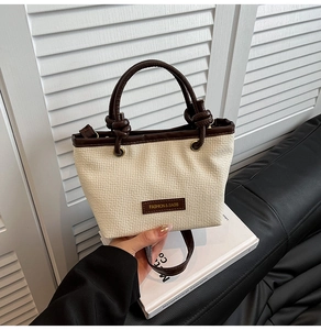 Detail of cream woven bucket bag with brown leather handles and adjustable shoulder strap